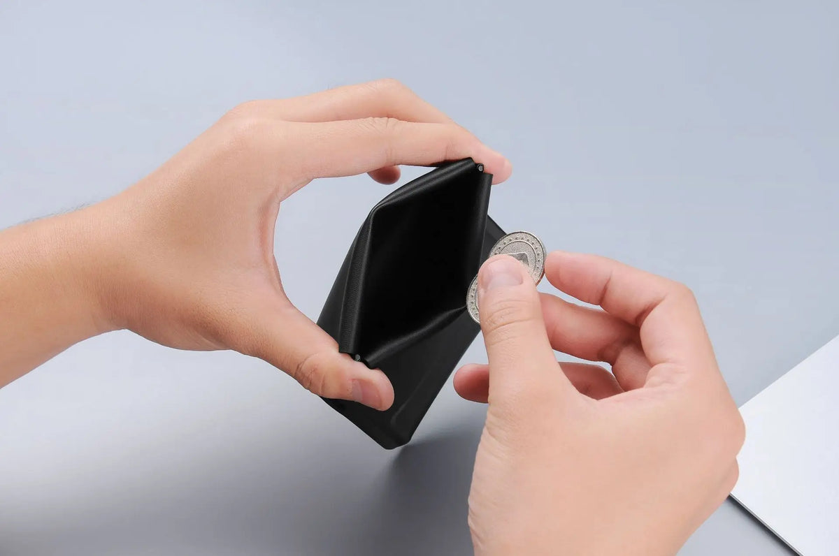 A hand is opening a black magnetic foldable ID card holder to reveal a coin inside.