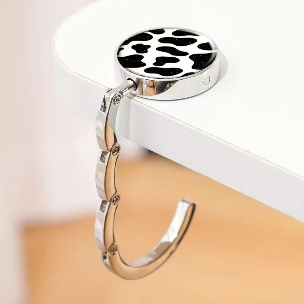 A silver metal round bag hanger with a black and white leopard print top is displayed on a white surface.