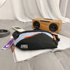 A black nylon chest rig bag is placed on a white sheet next to a wooden speaker and a smartphone.