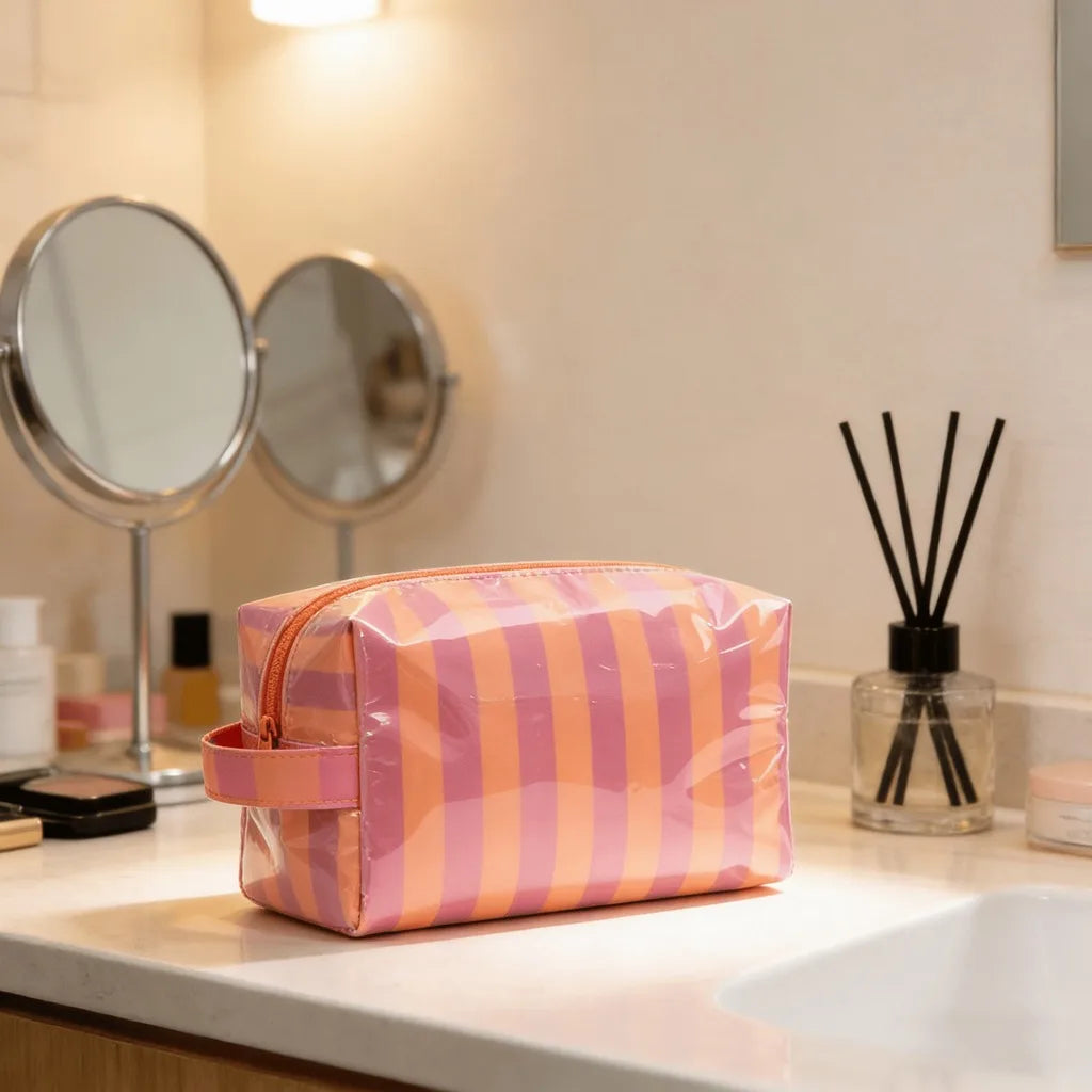 A pink and orange striped waterproof cosmetic bag resting on a white countertop in a bathroom setting.