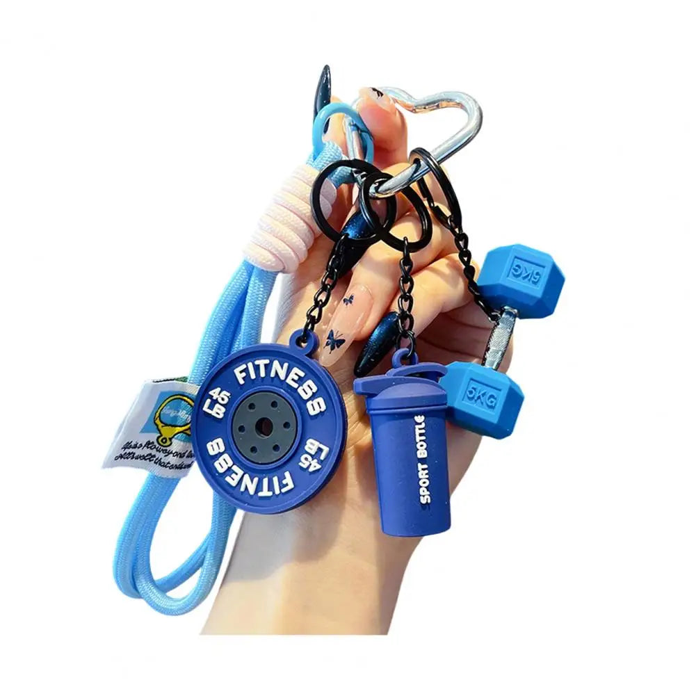 A hand holds a fitness keychain featuring a dumbbell and kettlebell charm.