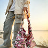 A person stands outdoors holding a pink and green camouflage canvas shoulder bag.