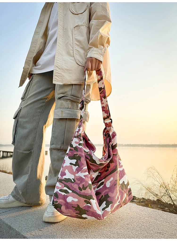 A person stands outdoors holding a pink and green camouflage canvas shoulder bag.