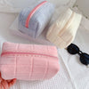 A pink quilted velvet cosmetic bag is shown next to light blue and cream colored bags on a white surface.