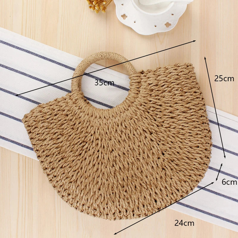 A handwoven straw moon bag with a top handle resting on a striped cloth next to a white cup.