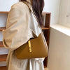 A woman wearing a beige coat is holding an elegant tan PU leather hobo shoulder bag.
