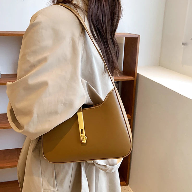 A woman wearing a beige coat is holding an elegant tan PU leather hobo shoulder bag.