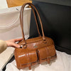 A brown leather vintage letter print crossbody bag is shown being held by a hand against a dark background.