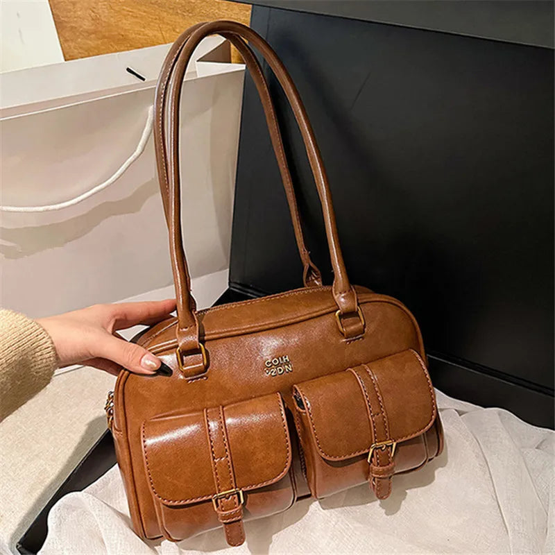 A brown leather vintage letter print crossbody bag is shown being held by a hand against a dark background.