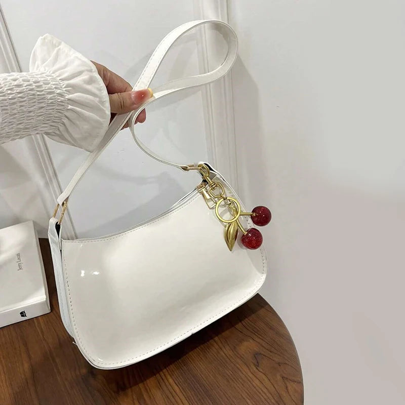 A white PU leather shoulder bag with a gold chain and cherry pendant is shown being held by a hand.