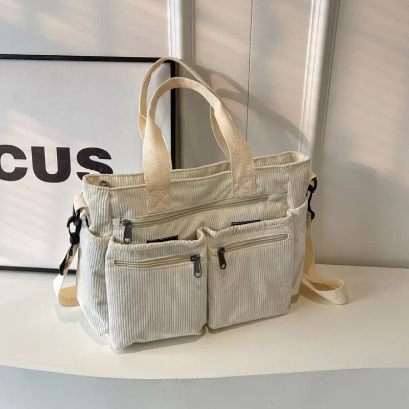 A cream textured corduroy tote bag with adjustable straps resting on a white surface.