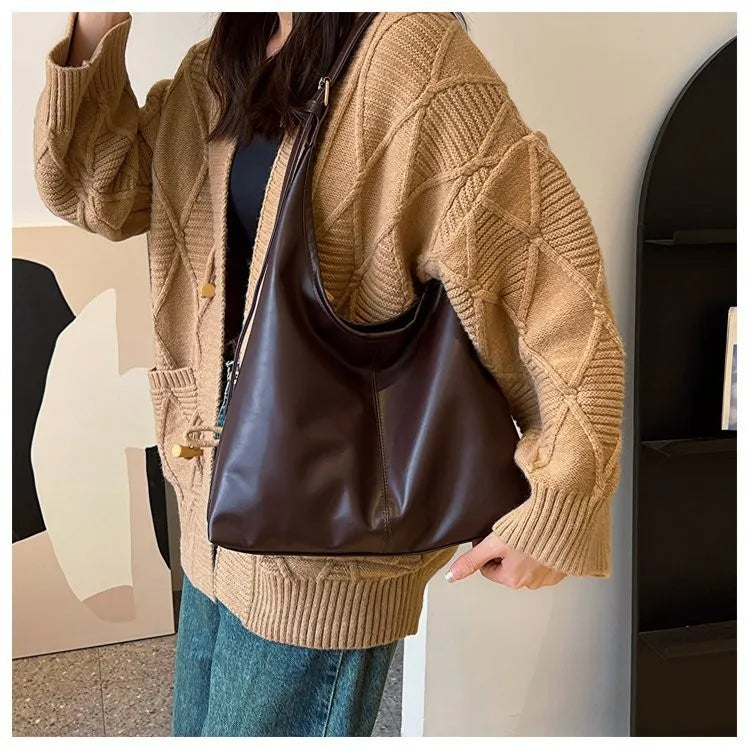 Eine Frau trägt einen beigen Strickcardigan und Jeans und hält eine braune Leder-Canvas-Tasche.