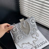 Silver rhinestone evening clutch bag displayed on a white surface next to a window blind.