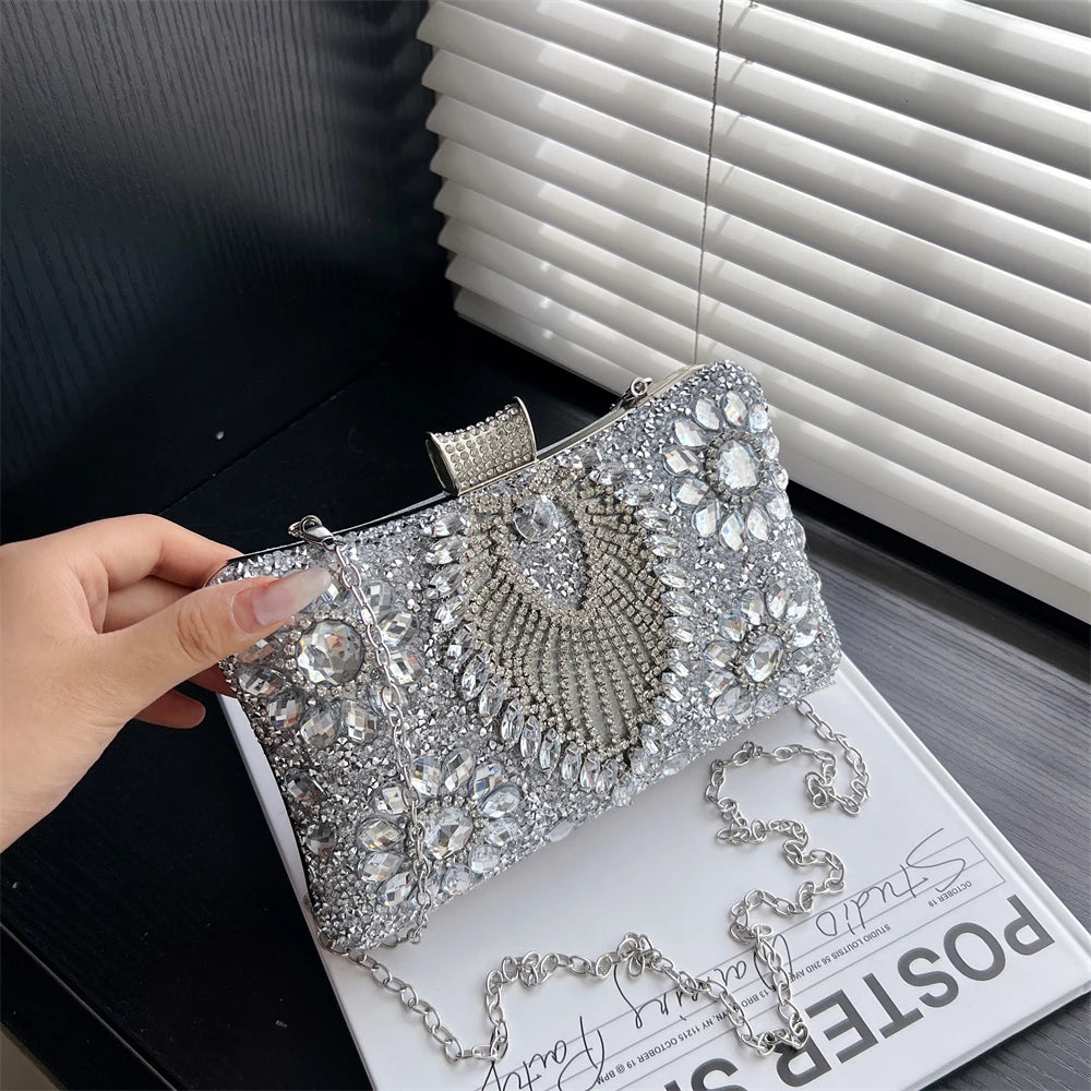 Silver rhinestone evening clutch bag displayed on a white surface next to a window blind.