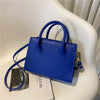 Sac à main en cuir PU bleu royal minimaliste avec poignée supérieure posé sur une surface blanche.