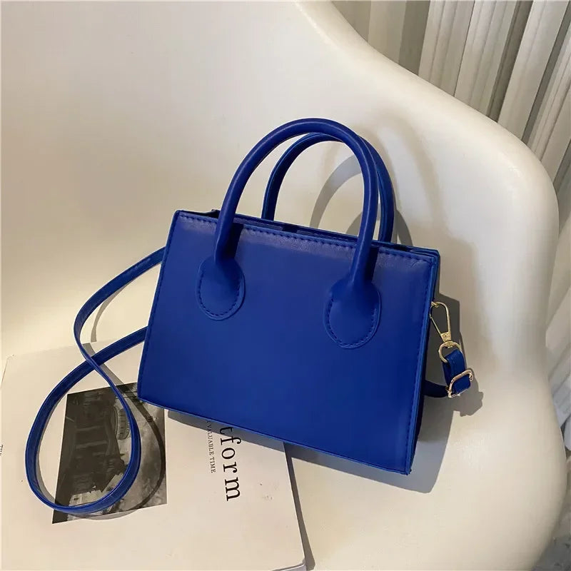 Sac à main en cuir PU bleu royal minimaliste avec poignée supérieure posé sur une surface blanche.