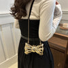 A woman wearing a black top and skirt holds an acrylic bow clasp mini handbag with a gold chain strap.