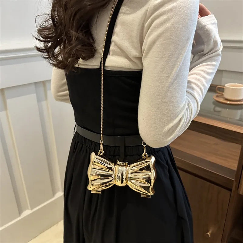 A woman wearing a black top and skirt holds an acrylic bow clasp mini handbag with a gold chain strap.