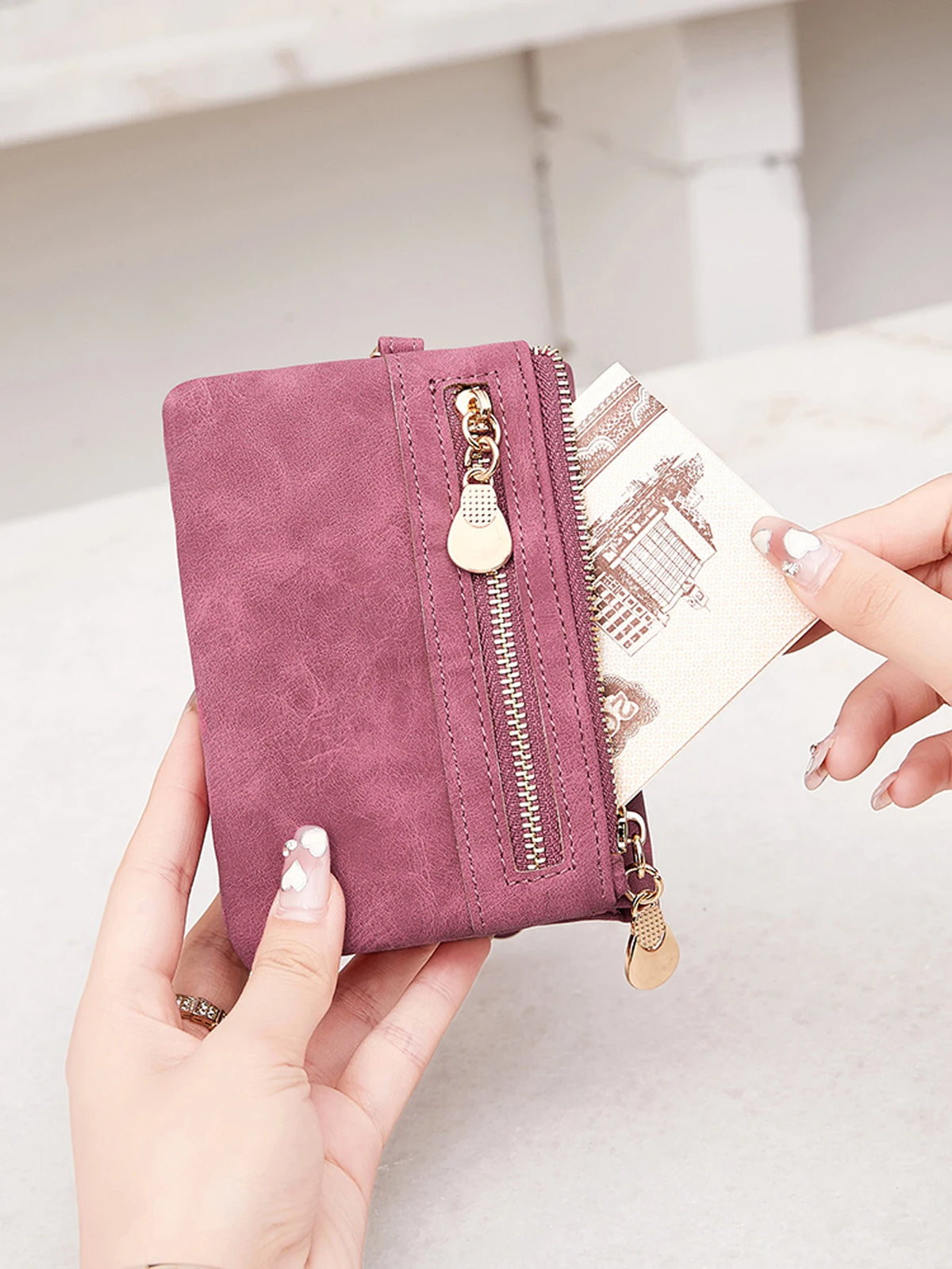 Una mano sostiene una cartera de cuero PU plegable retro mauve con herrajes dorados contra un fondo claro.