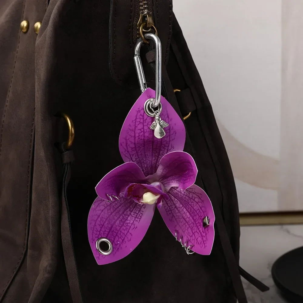 A purple orchid flower keychain hanging from a zipper pull on a dark brown backpack.