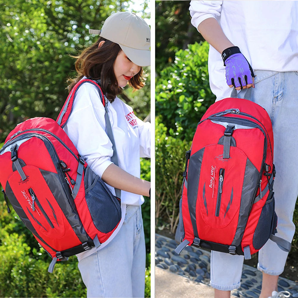 A woman wearing a white shirt and jeans is shown carrying a red and black waterproof hiking backpack outdoors.