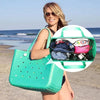 A woman holds a bright green waterproof beach bag organizer with dividers against a beach background.