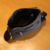 A dark blue patterned sling bag with a black lining and silver zippers resting on a wooden surface.