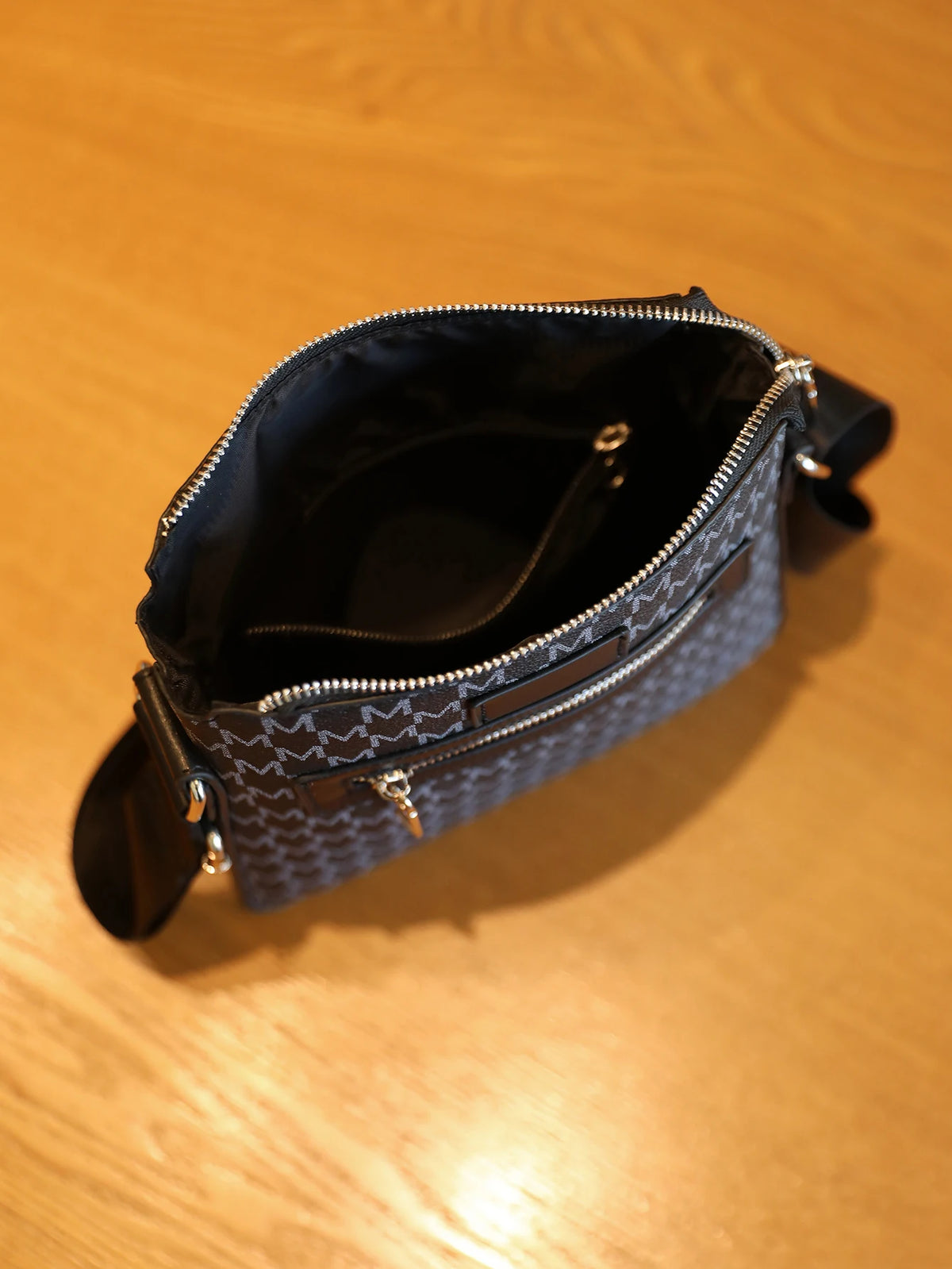 A dark blue patterned sling bag with a black lining and silver zippers resting on a wooden surface.