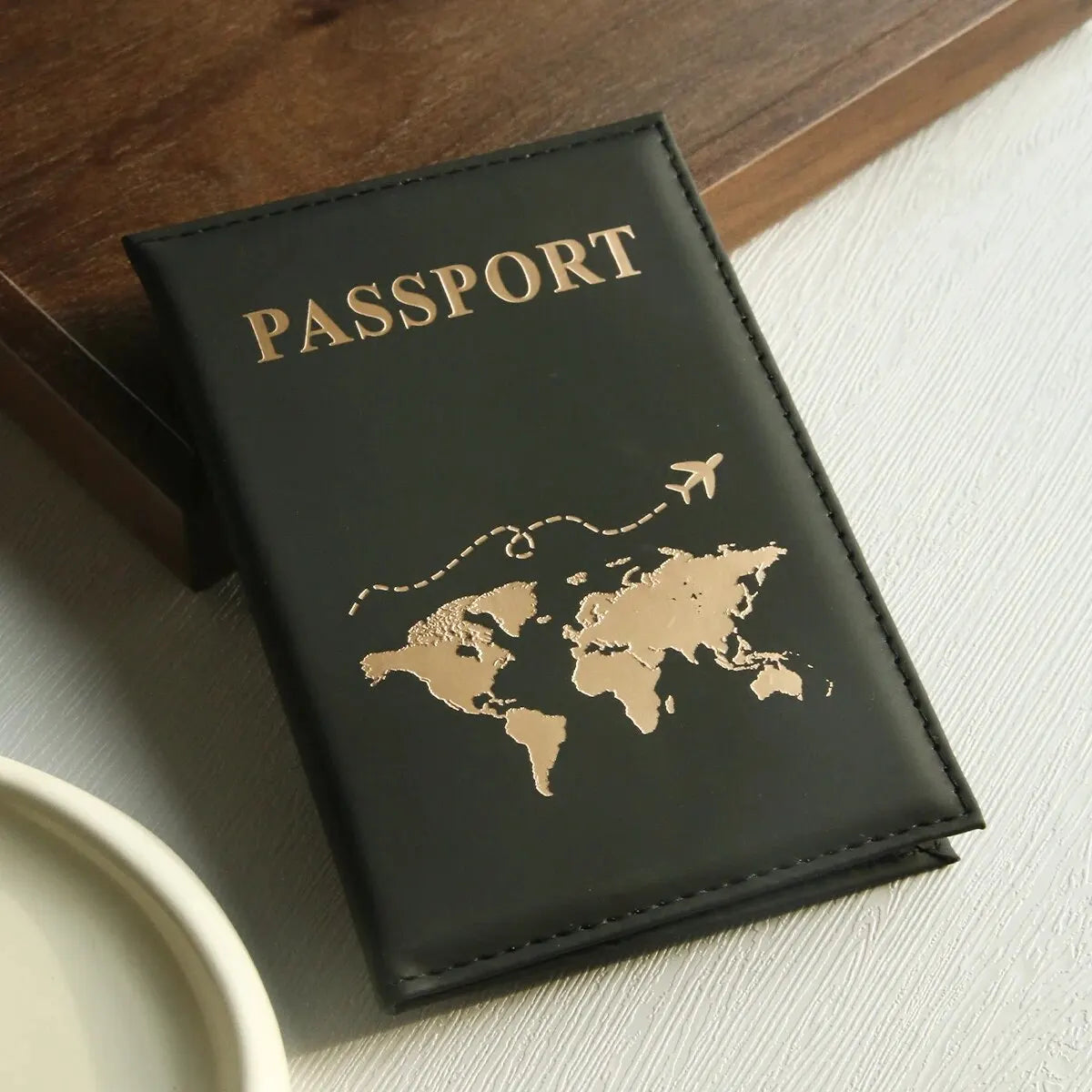 Schwarzes Leder-Reisepass-Halter mit Goldfolgedruck einer Weltkarte und dem Wort PASSPORT.