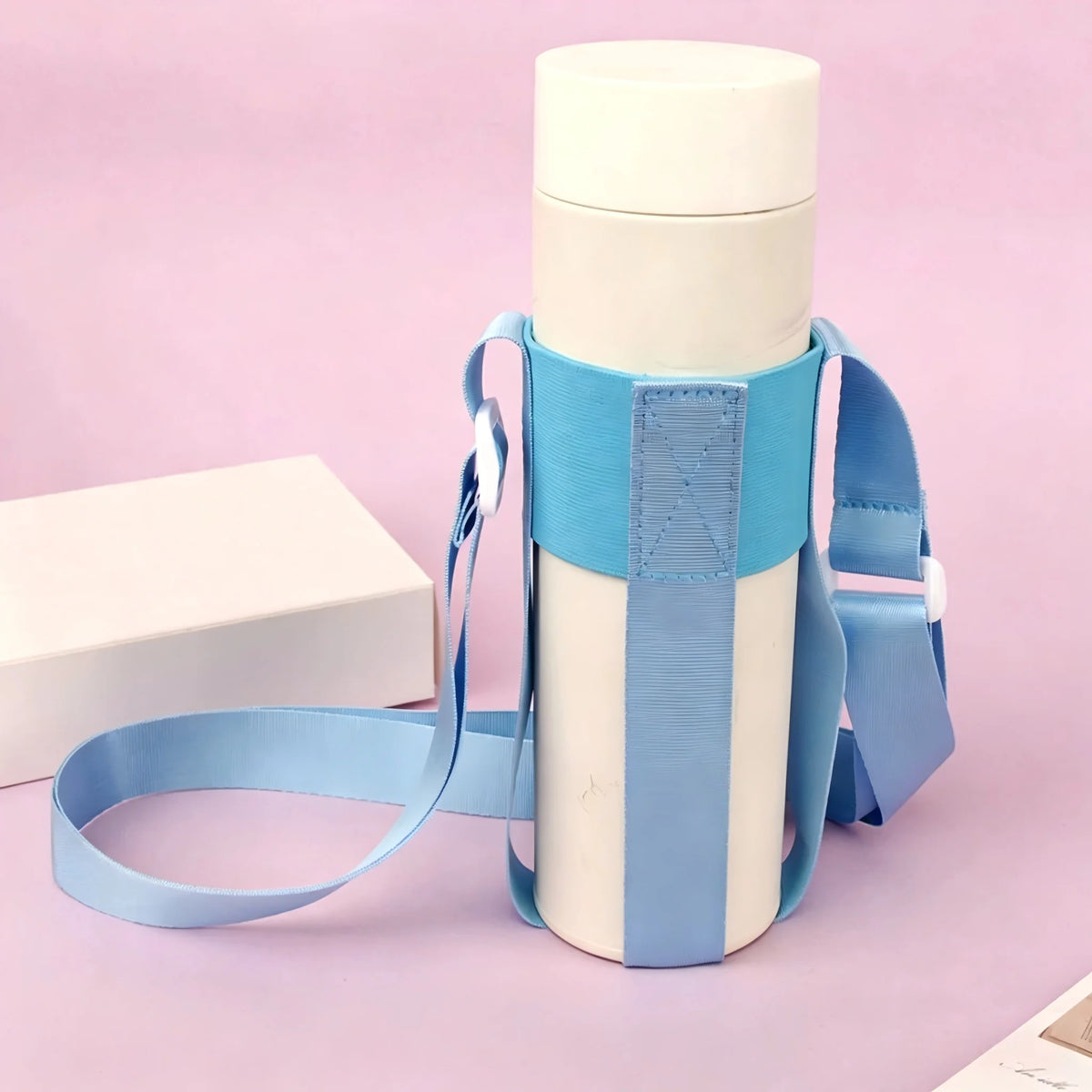 A light blue water bottle is shown with a matching sling bag attached, set against a pink background.
