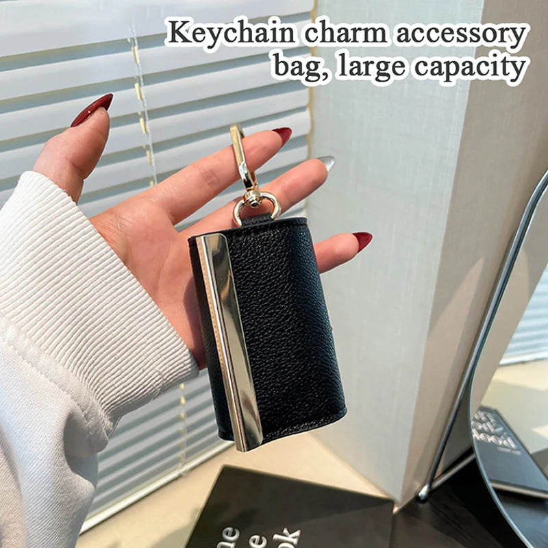 A hand holds a black and silver cloth storage pouch keychain accessory bag.