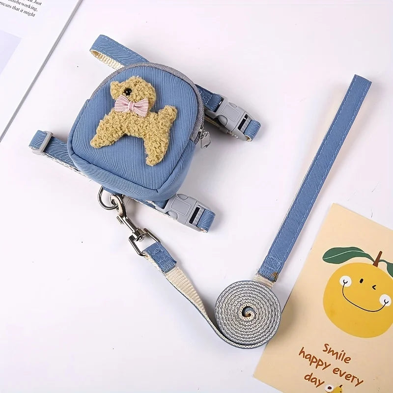 A light blue adjustable dog vest with a backpack and leash featuring a small teddy bear charm.