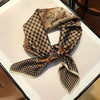 A patterned silk hair scarf featuring a gold and black paisley design tied in a bow.