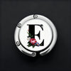 A silver, round letter E hanger hook with a floral design on a dark background.