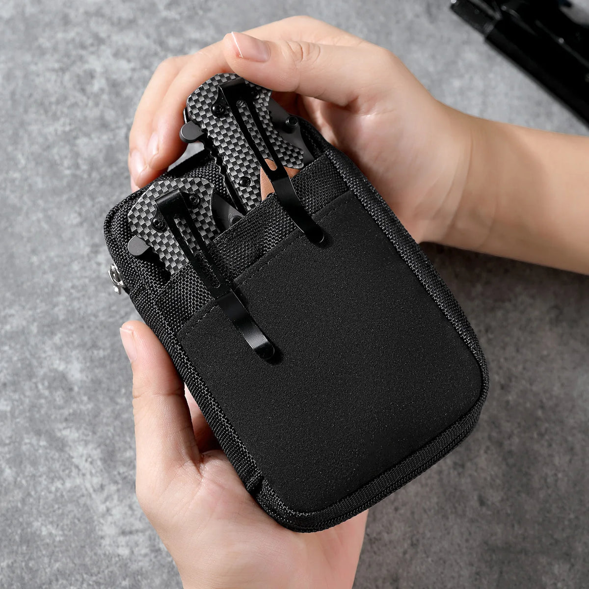 A hand holds a black portable multi-tool organizer pouch with a mesh insert for outdoor gear.