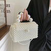 A close-up of a white pearl beaded clutch bag with a silver chain strap held by a person.