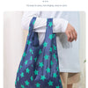 A dark blue reusable shopping bag with a widened shoulder strap is shown being carried by a person.