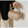 A hand holds a beige leather shoulder bag with gold hardware against a white wall.
