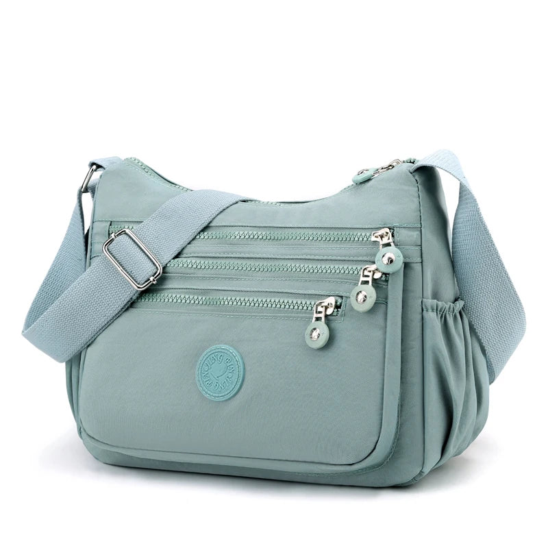 A light blue waterproof nylon crossbody shoulder bag with zippered pockets and a circular logo.