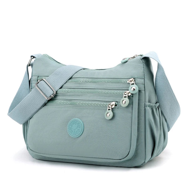 A light blue waterproof nylon crossbody shoulder bag with zippered pockets and a circular logo.