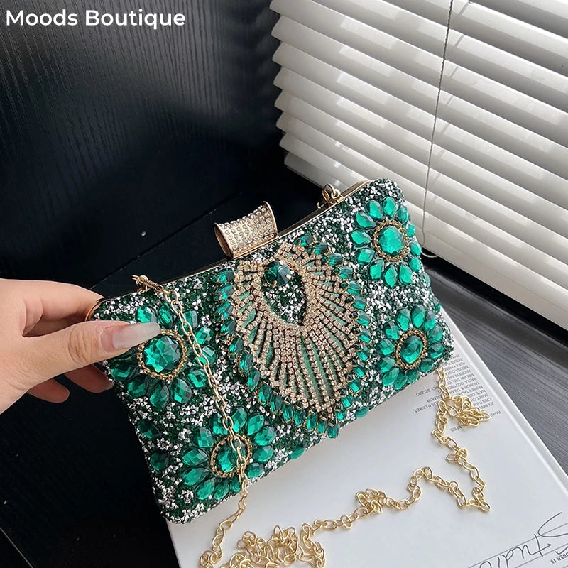 A sparkling emerald green rhinestone evening clutch bag with gold chain detailing is shown on a white surface.