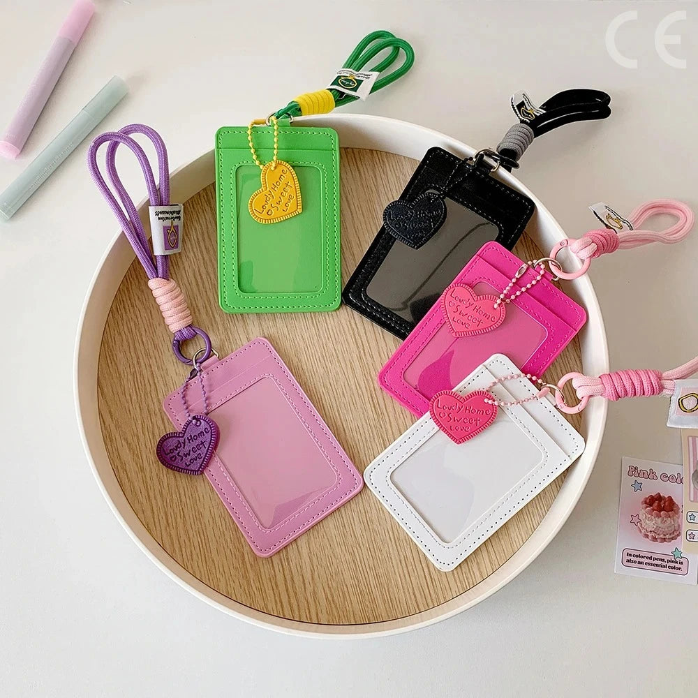 A collection of pink and green PU credit card and ID holders with various keychain attachments arranged on a wooden plate.
