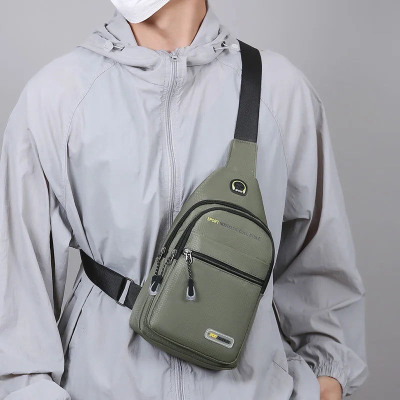 A man wearing a light gray jacket is holding a olive green multi-pocket shoulder bag.