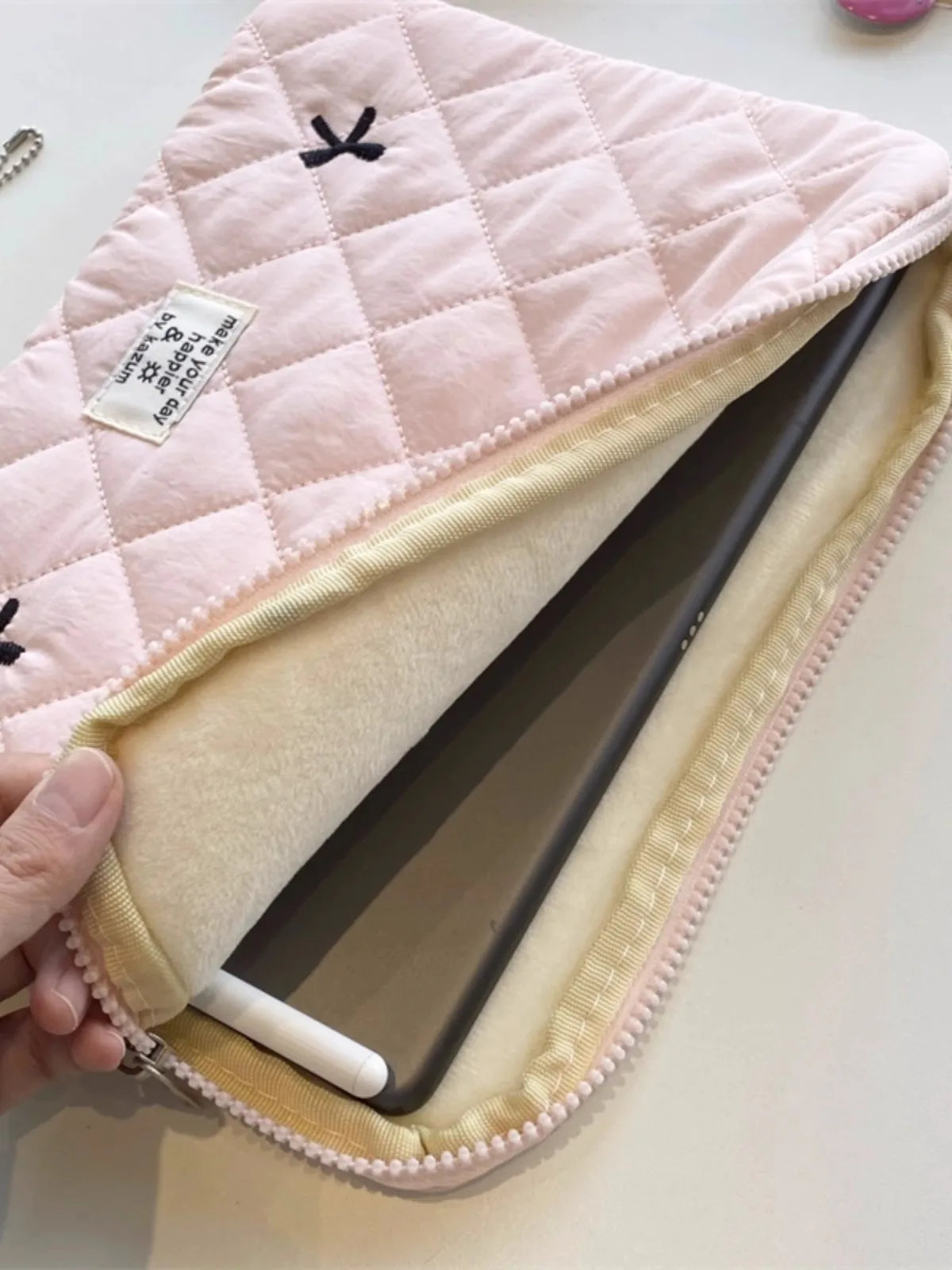 A pink quilted laptop sleeve with a light beige lining and a small tag is shown being held.