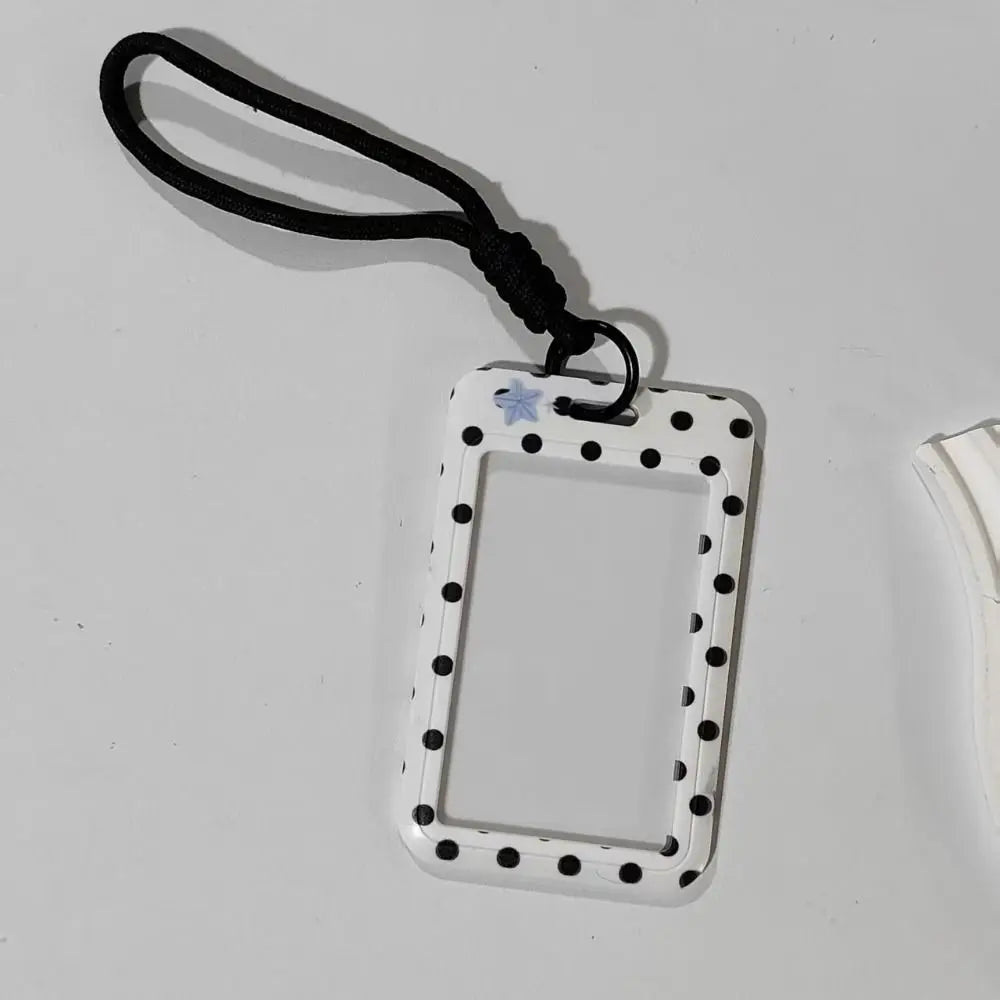 A white card holder with a rectangular frame and black polka dots is attached to a black lanyard.