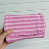 A hand holds a pink and white striped Y2K makeup bag with a zipper, made of cotton toiletry pouch material.