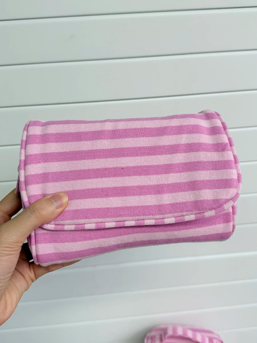 A hand holds a pink and white striped Y2K makeup bag with a zipper, made of cotton toiletry pouch material.