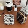 A leopard print PU leather jewelry storage box next to a coffee cup and glass on a brown surface.