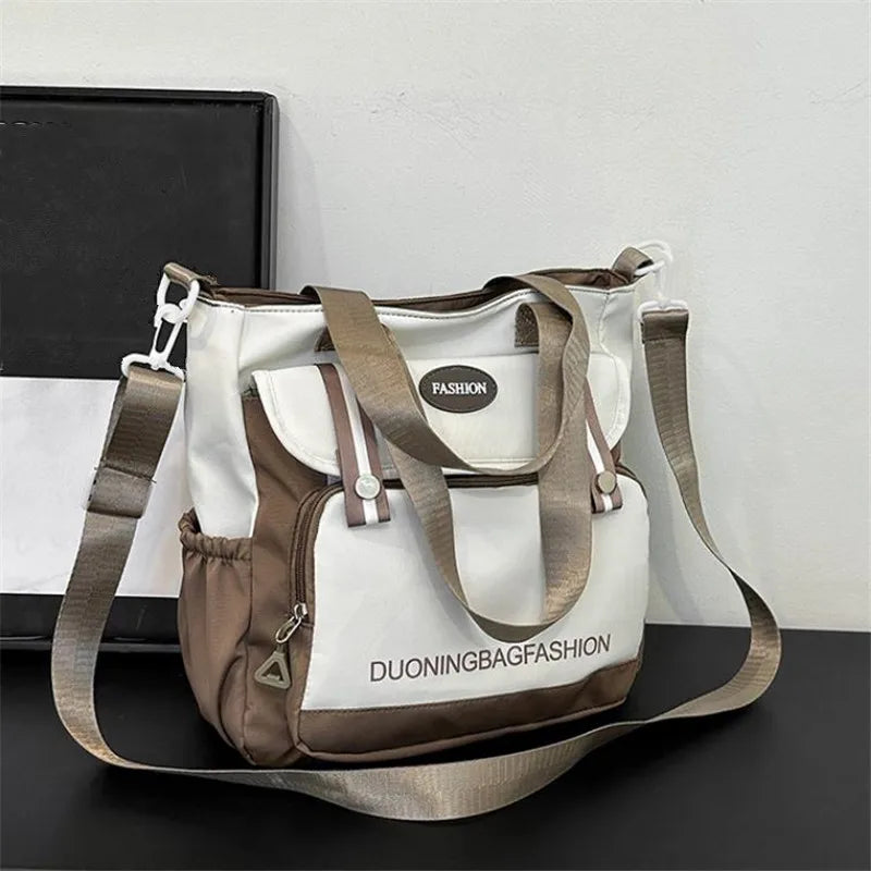 Beige und weißer Nylon-Bucket-Totebag mit braunen Riemen auf dunkler Oberfläche.