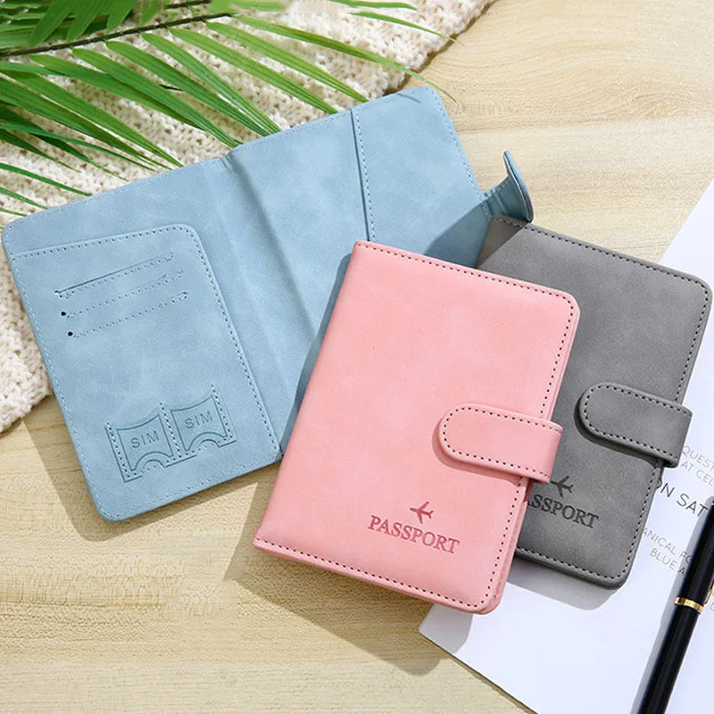 A pink passport holder cover and a gray passport holder cover are displayed on a wooden surface.